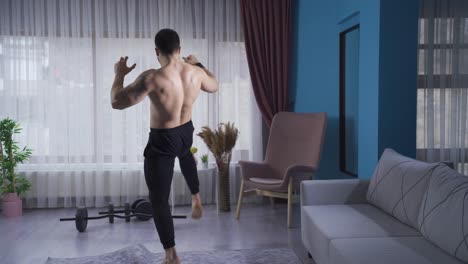 Young-athlete-doing-kickboxing-against-the-air-at-home-with-his-back-turned.